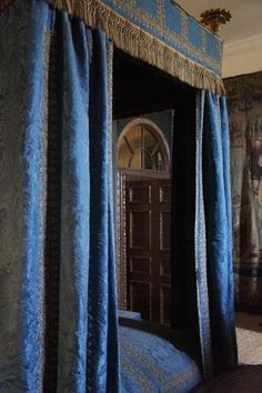 a canopy bed with blue and gold drapes on it's sides in a bedroom