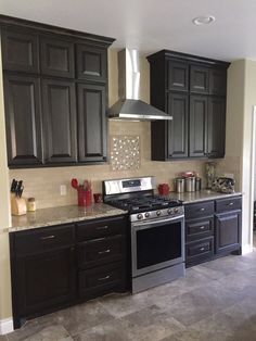 a kitchen with black cabinets and stainless steel stove top oven, range hood over island