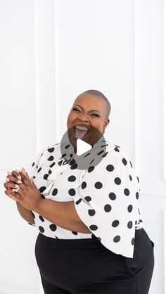 a woman in black and white polka dot shirt holding her hands out to the side