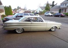 an old car is parked on the side of the road in front of some houses