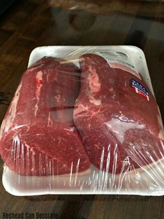 two raw steaks wrapped in plastic on a wooden table