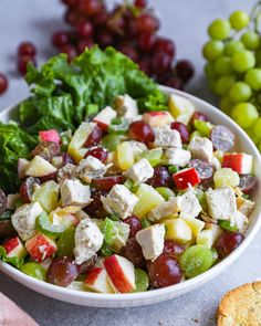 a white bowl filled with grapes and chicken salad next to some crackers on the side