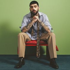 a man sitting on a red chair with his hands in his pockets and tie around his neck