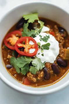 a white bowl filled with taco soup topped with sour cream and cilantro