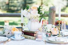 the table is set with tea cups, books and flowers in vases on it