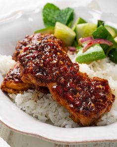 a white plate topped with rice and meat covered in sauce next to cucumbers