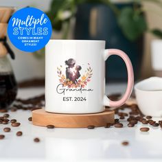 a white coffee mug with a pink handle sits on a wooden coaster surrounded by coffee beans