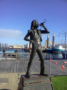 there is a statue of a woman holding a microphone in front of the water and boats