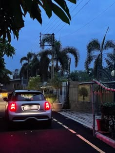 a car is parked on the street in front of a house at night with palm trees