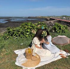 two women sitting on a blanket in front of the ocean, one holding an umbrella