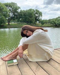 a woman sitting on a dock next to a body of water