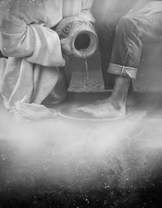 black and white photograph of a person sitting next to a fire hydrant with water pouring out of it