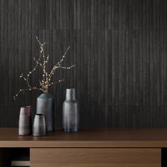 three vases sitting on top of a wooden table in front of a black wall