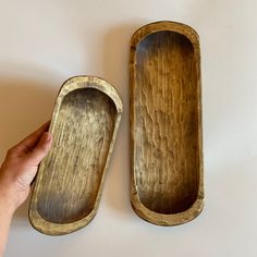 two wooden trays sitting next to each other on a white surface with one being held up by a person's hand