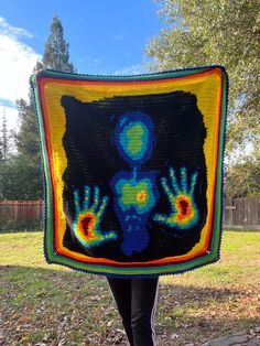 a woman is holding up a crocheted blanket in the shape of a human figure