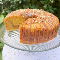 a bundt cake with icing and nuts is on a glass platter next to a green bush