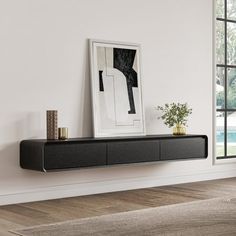 a black shelf sitting on top of a wooden floor next to a window with a painting hanging above it