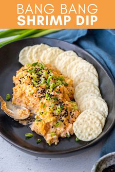 a black plate topped with food next to a bowl of rice and some green onions