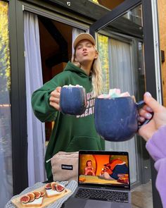 a woman in a green hoodie holding two bowls of food