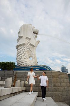 a man and woman shaking hands in front of a large statue with water spouting from it