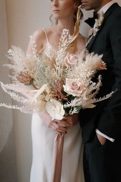 the bride and groom are holding their wedding bouquets in front of each other with feathers on them