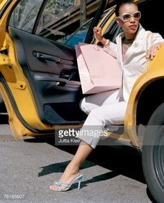 a woman sitting in the back of a yellow car with shopping bags on her feet