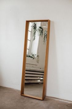 a mirror sitting on the floor in front of a white wall with plants growing out of it