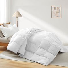 a bed with white comforter and pillows on top of it in a room next to a window