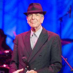 an older man in a suit and hat holding a microphone while standing next to a piano