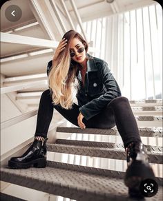 a woman sitting on some stairs with her hair blowing in the wind and wearing black boots