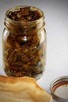 a jar filled with food next to a slice of bread on a white table top