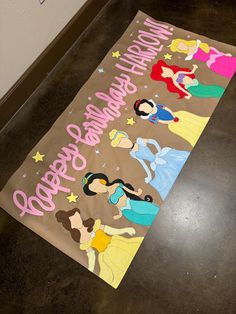 a birthday banner with princesses on it sitting on the floor next to a wall