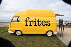 a yellow food truck with the word frites written on it's side in front of some grass