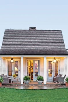 a small white house with two front porches and chairs on the grass in front of it