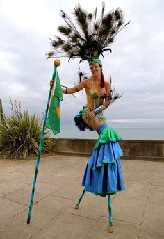 a woman in costume holding a pole and feathered headdress on the beach