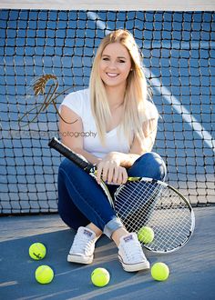 a woman sitting on the ground holding a tennis racquet and four tennis balls