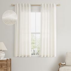 a living room with white curtains and a chair in front of a window that has a round light fixture on it