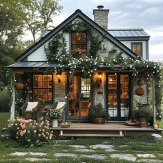 a small house with lots of greenery on the front porch and covered in flowers