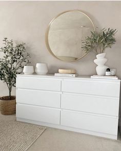 a white dresser sitting in front of a mirror and potted plant on top of it