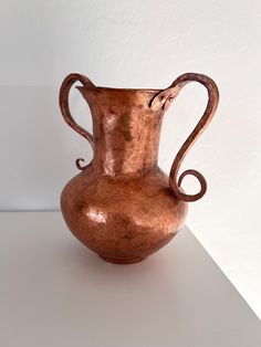 a copper colored vase sitting on top of a white table next to a white wall