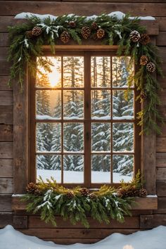 a window decorated with evergreen leaves and pine cones in front of snow - covered trees