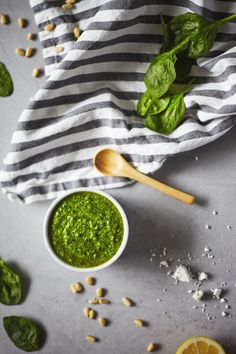 spinach pesto sauce in small bowls with wooden spoons and fresh basil leaves