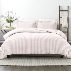 a bed with pink and white striped bedspread in a small room next to a potted plant