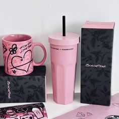 a pink coffee cup sitting on top of a box next to a pink mug and other items