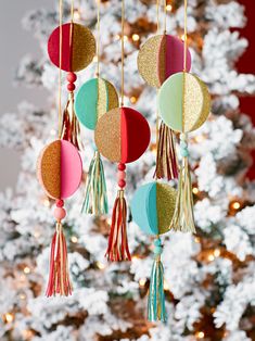 some ornaments hanging from a christmas tree in front of a white christmas tree with lights