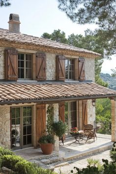 a stone house with wooden shutters on the front and side windows, surrounded by greenery