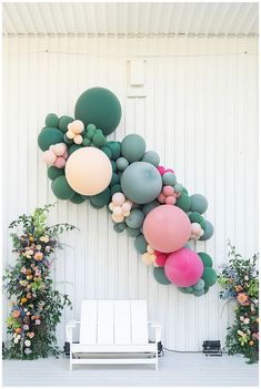 a bunch of balloons hanging on the side of a white wall next to a bench