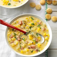 two bowls filled with corn chowee next to crackers on a white tablecloth