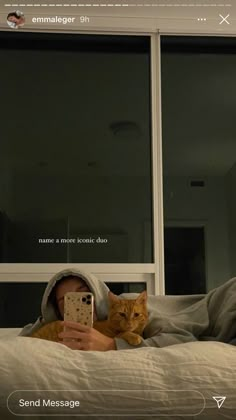 a person laying in bed with a cat on their lap looking at a cell phone