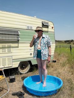 a woman standing on top of a blue pool next to an old fashioned camper